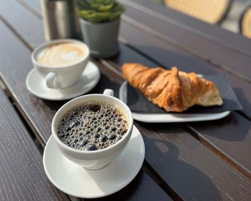 En kaffelatte, en cappuccino og en croissant står på et av bordene på uteserveringen.